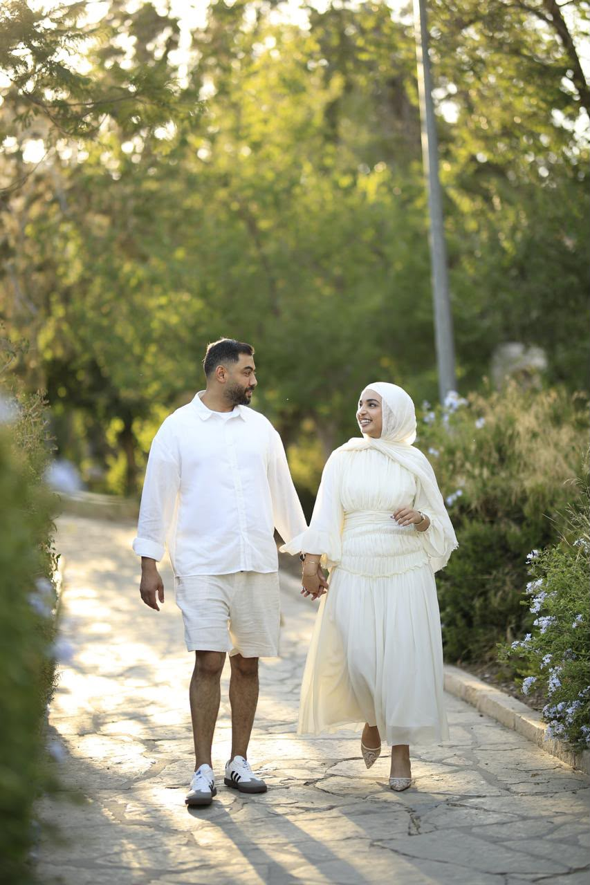Basel and Rafeef walking hand in hand on a garden path